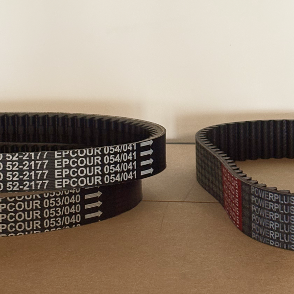 Three black and toothed belts on a wooden surface. The belt on the right reads "Movendis POWERPLUS."